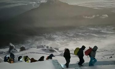 A group of hikers enjoying a snowy mountain view, surrounded by white snow and blue skies.