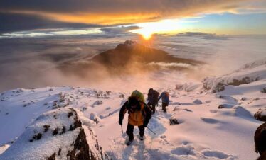 A group of people hiking up a snowy mountain as the sun sets.