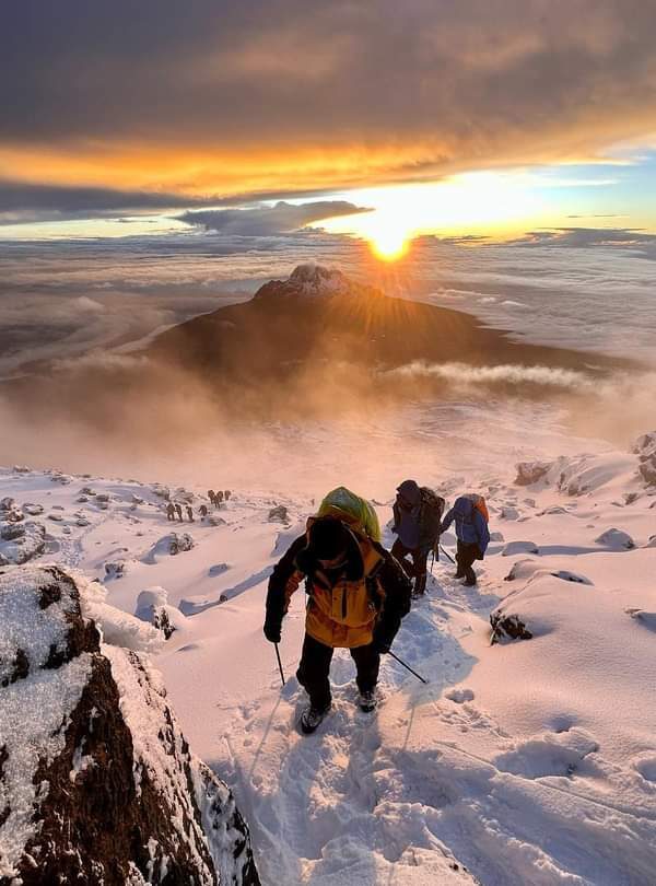 A group of people hiking up a snowy mountain as the sun sets.